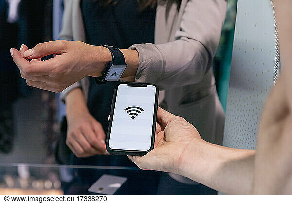 Woman doing contactless payment through smart watch near mobile phone at clothes store