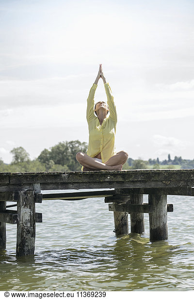Woman doing lotus pose yoga on jetty at the lake  Ammersee  Upper Bavaria  Germany