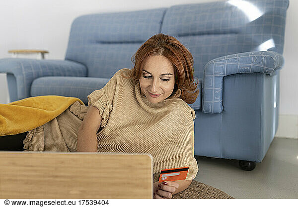 Woman doing online payment on laptop holding credit card at home