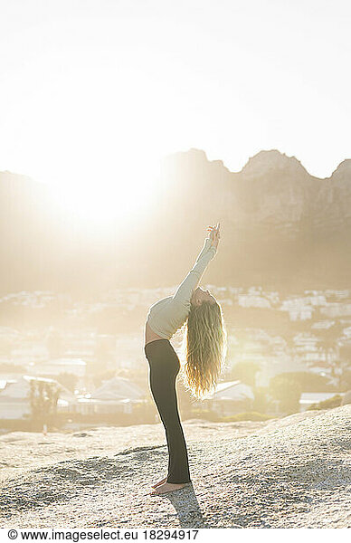 Woman doing stretching exercise on rock at sunrise