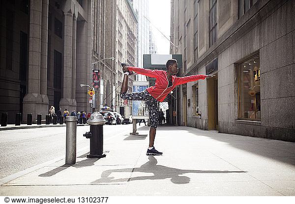 Woman doing yoga in king dancer pose on sidewalk in city