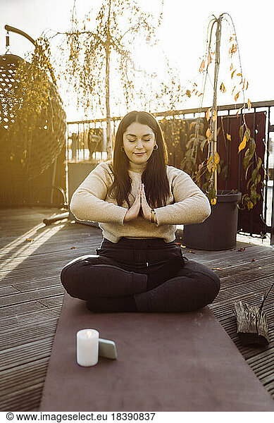 Woman doing yoga while sitting with hands clasped on exercise mat at terrace