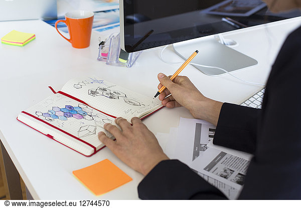 Woman drawing into notebook at desk in office
