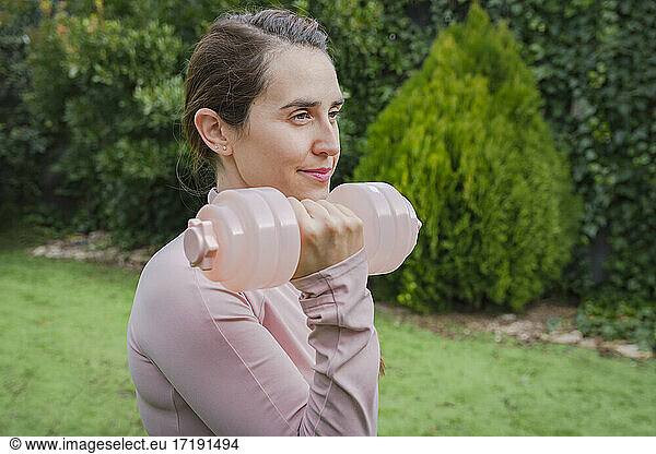 Woman dressed in pink lifting dumbbell in yard  home fitness