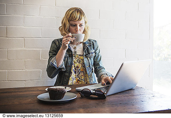 Woman drinking coffee while using laptop computer in cafe