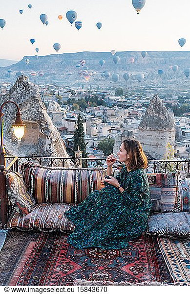 Woman drinking early morning tea with hot air balloons in Cappadocia