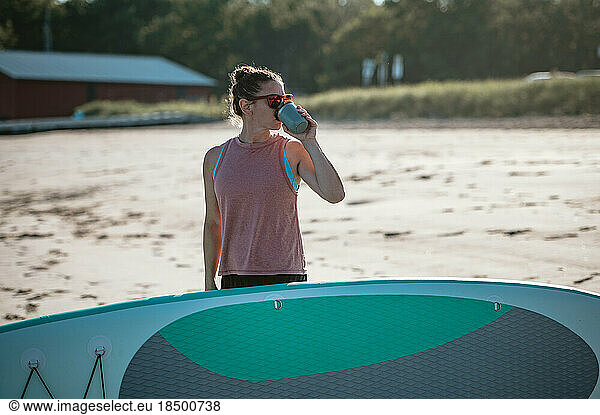 Woman drinking from coffee mug with paddleboard