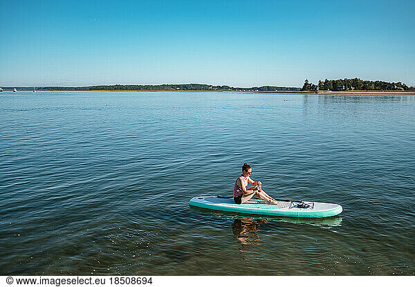 Woman drinking from mug on stand-up paddleboard on ocean