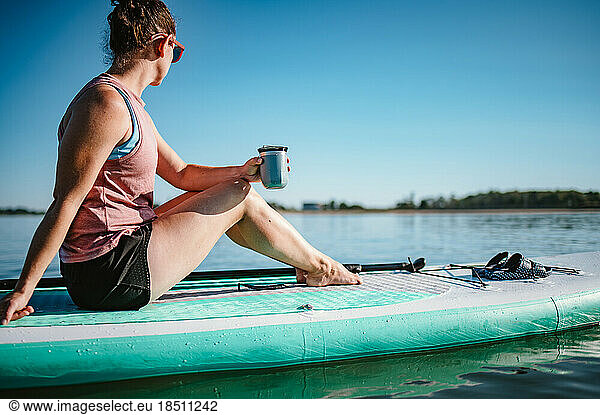 Woman drinking from mug on stand-up paddleboard on ocean