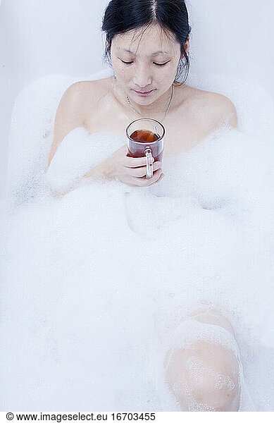 Woman drinking hot beverage while taking a bubble bath
