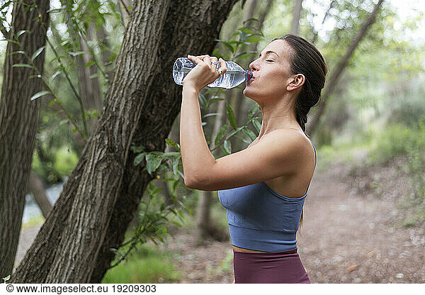 Woman drinking water near tree at forest