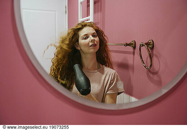 Woman drying hair looking in mirror at home