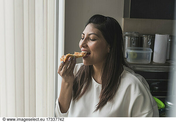 Woman eating pizza by curtain at home