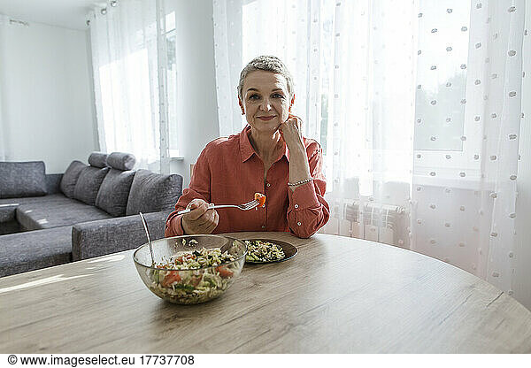 Woman eating salad at wooden table at home