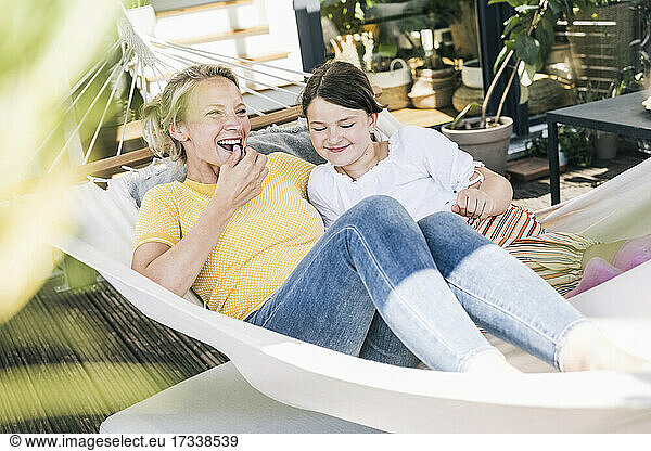 Woman eating while lying with girl in hammock at balcony