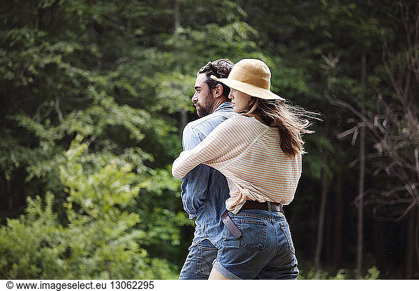 Woman embracing man while standing against trees