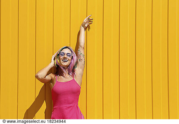 Woman enjoying music listening through wireless headphones in front of yellow wall