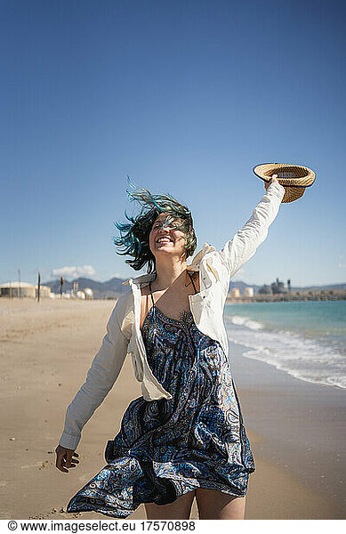 Woman enjoying the wind on the beach with a hat in hand