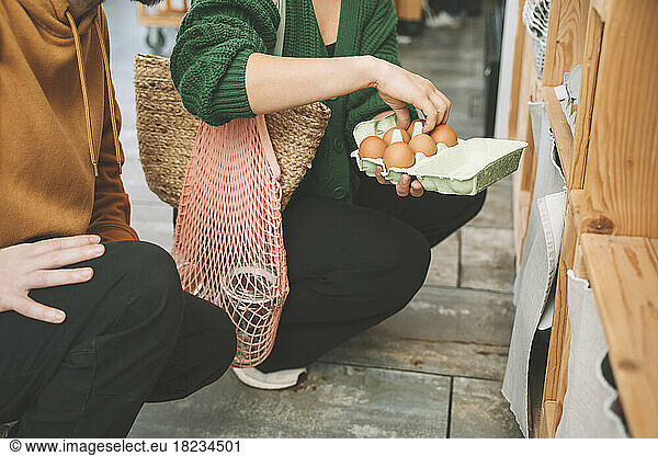 Woman examining eggs in carton by man at shop