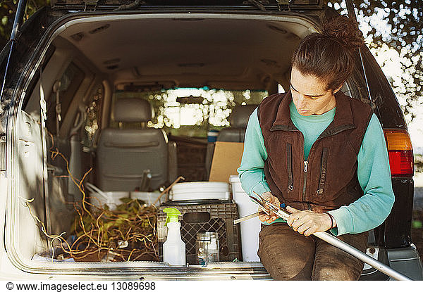 Woman examining gardening tool while sitting in car trunk
