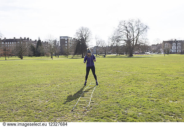 Woman exercising  doing speed ladder drill in sunny park