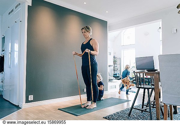 Woman exercising with resistance band by girls in living room