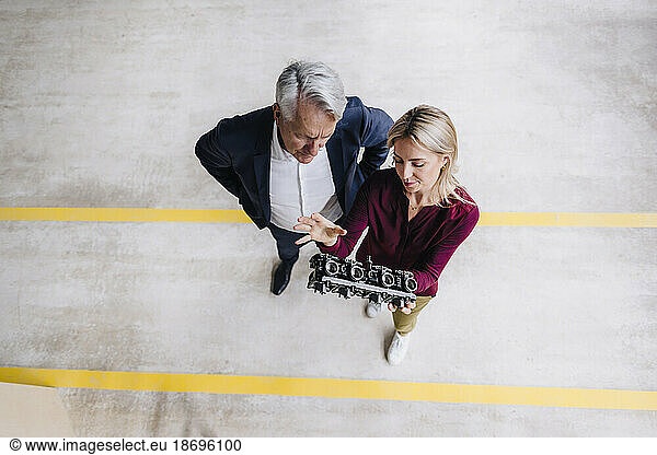 Woman explaining machine part to businessman standing in factory