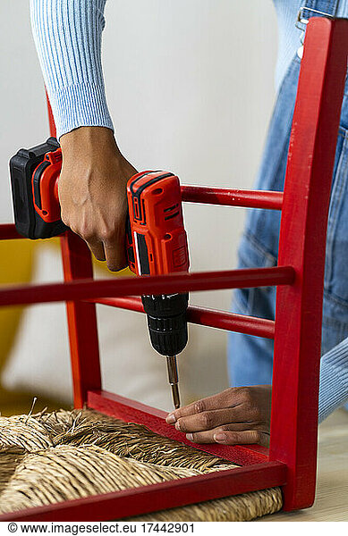 Woman fastening chair with electric screwdriver at home