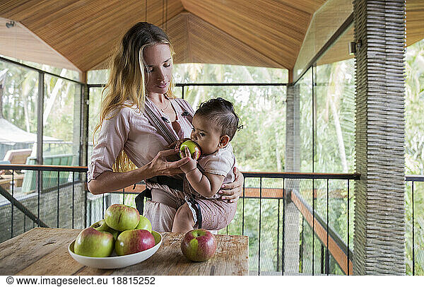 Woman feeding apple to daughter at home