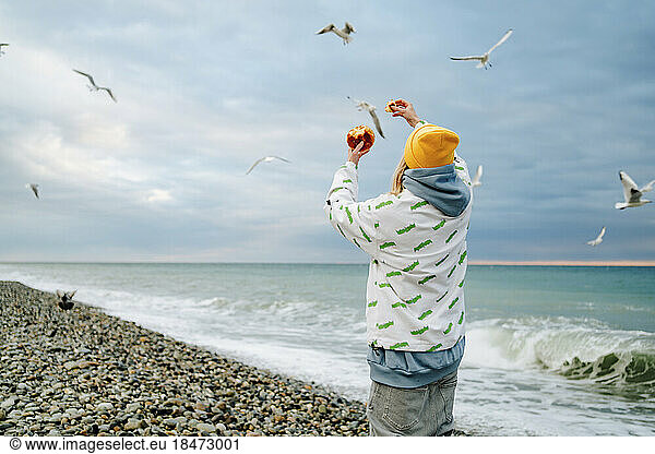 Woman feeding seagulls at seashore