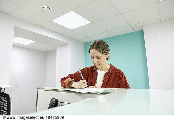 Woman filling form at reception in medical clinic