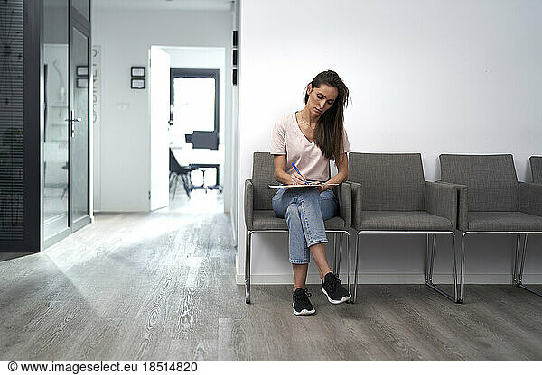 Woman filling form sitting on chair in waiting room