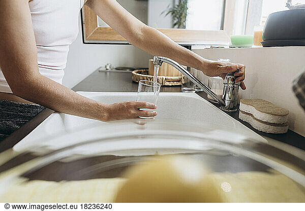 Woman filling glass with tap water in kitchen