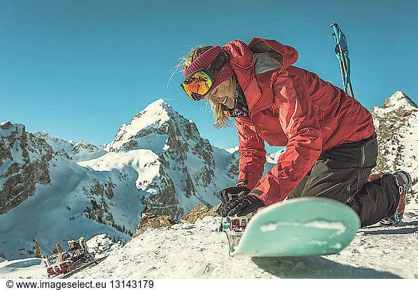 Woman fixing ski against snowcapped mountains