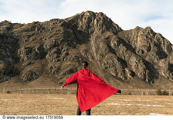 Woman from back in a red bathrobe runs next to the mountain