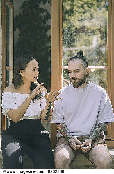 Woman gesturing and talking with hipster boyfriend sitting on window sill