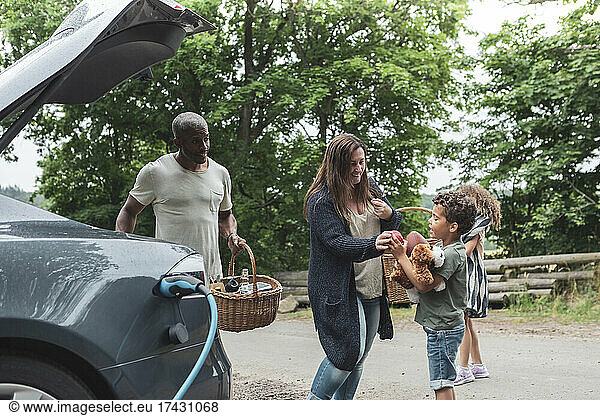 Woman giving apple to son while standing by electric car