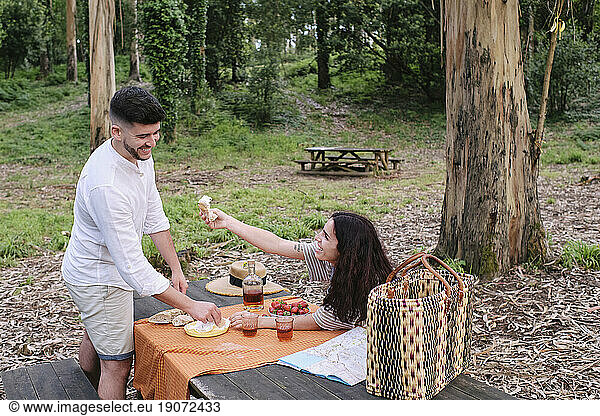 Woman giving food to boyfriend standing at table in forest