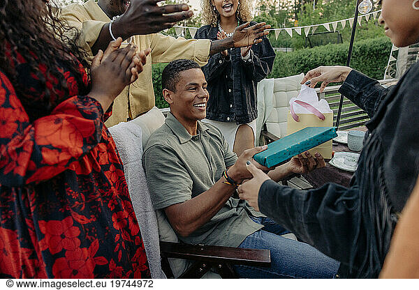 Woman giving gifts to smiling male friend during birthday celebration in back yard