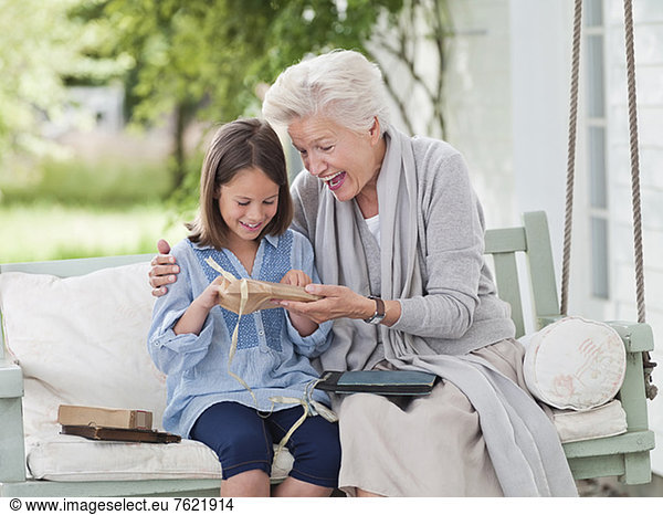 Woman giving granddaughter present in porch swing