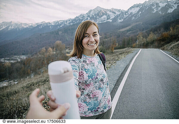 Woman giving insulated drink container to friend on mountain