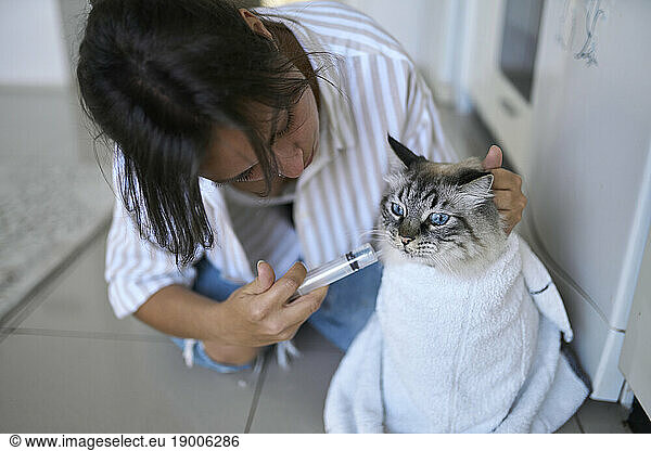 Woman giving medicine to cat at home