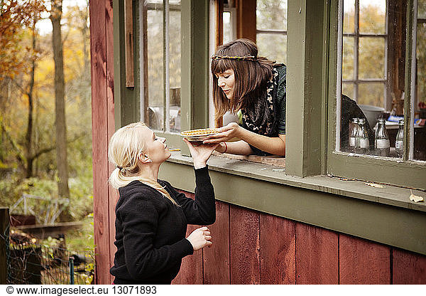Woman giving tart to friend while leaning on window