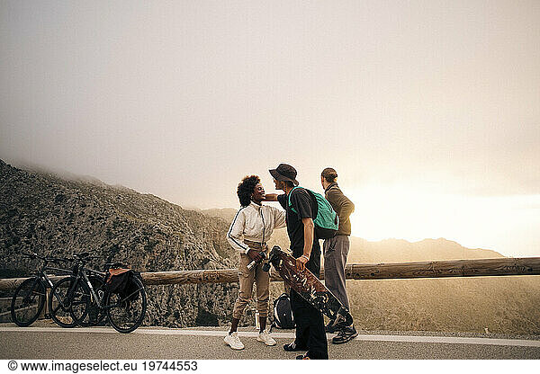 Woman greeting male friend holding skateboard while standing on road against sky
