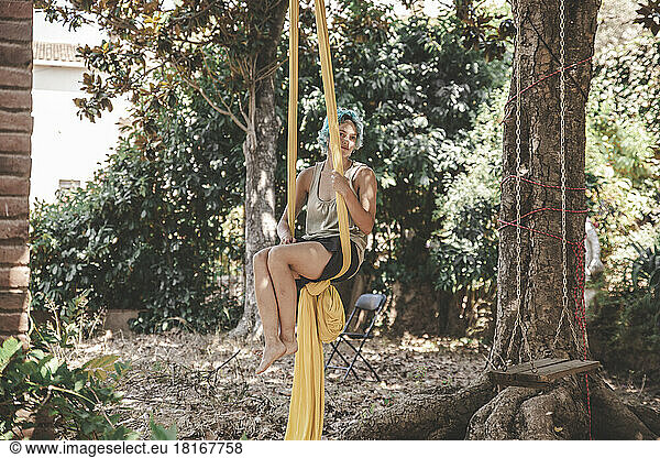 Woman hanging on aerial silk practicing acroyoga by tree