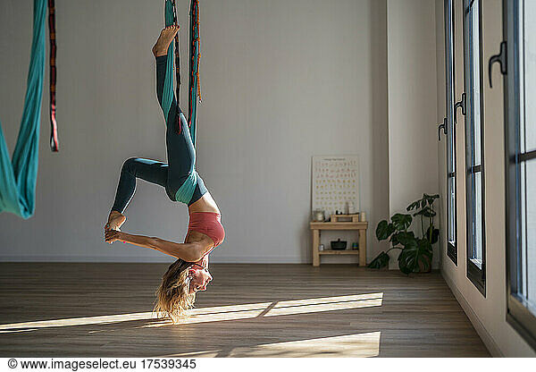 Woman hanging upside down on aerial silk practicing yoga at health club