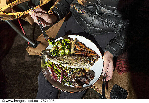 Woman has camp dinner with trout  brussel sprouts and carrots.