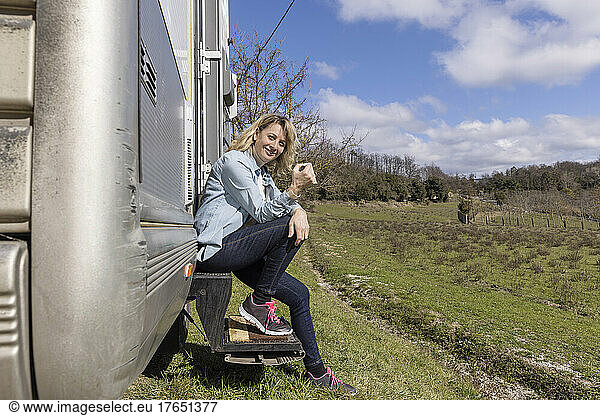 Woman having coffee sitting on doorstep of motor home