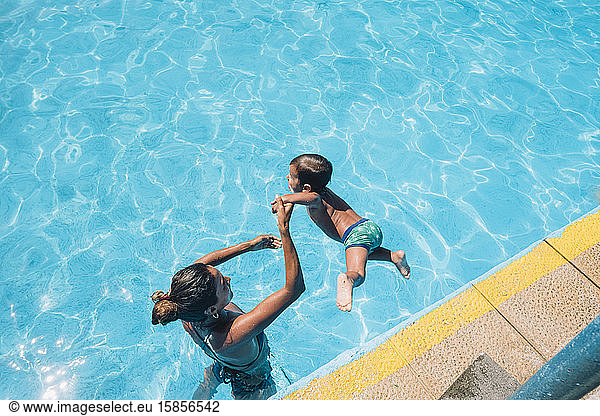 Woman helping child jumping into a pool