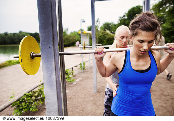 Woman helping friend in lifting barbell at park